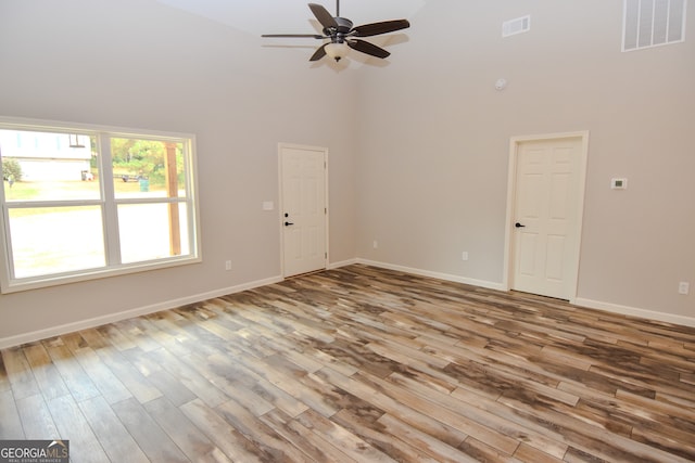 spare room with a towering ceiling, ceiling fan, and light hardwood / wood-style floors