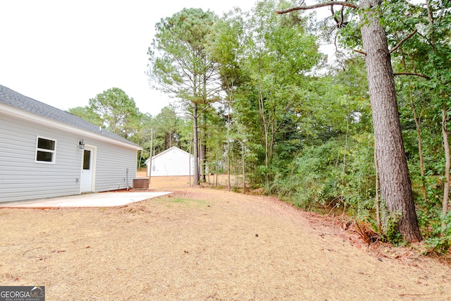 view of yard with an outdoor structure, a garage, a patio area, and central AC