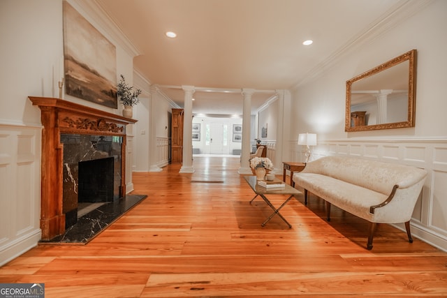 living area featuring crown molding, light hardwood / wood-style floors, decorative columns, and a fireplace