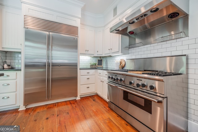 kitchen with wall chimney exhaust hood, light hardwood / wood-style floors, high quality appliances, ornamental molding, and white cabinets