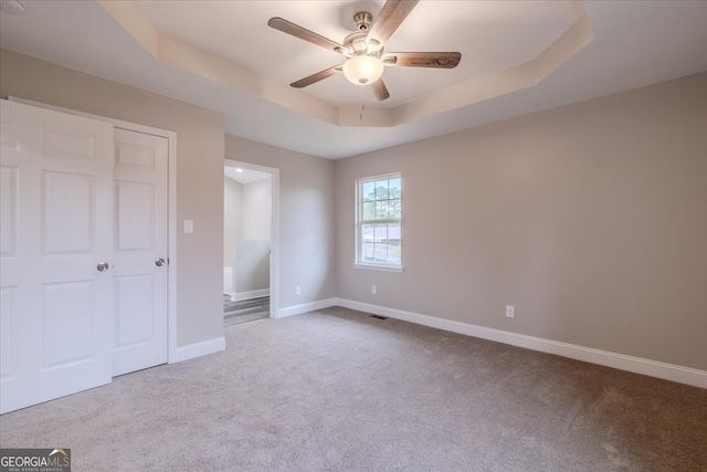 unfurnished bedroom with a raised ceiling, light colored carpet, ceiling fan, and a closet