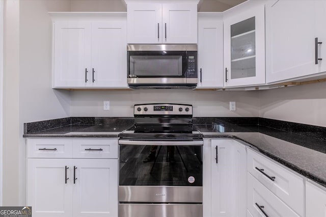 kitchen with appliances with stainless steel finishes, dark stone countertops, and white cabinetry