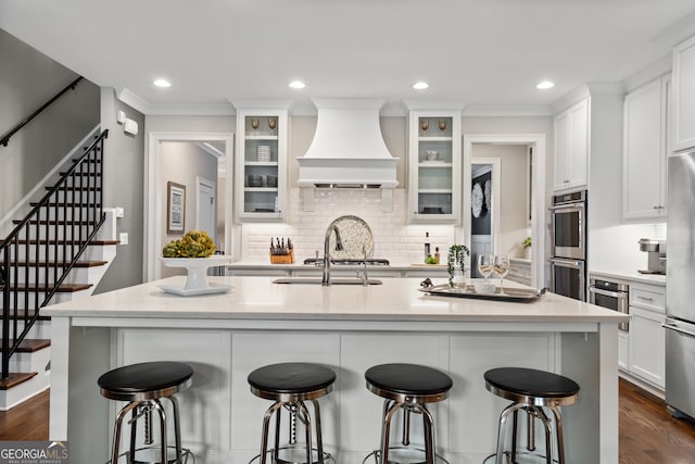 kitchen with white cabinets, a center island with sink, dark wood-type flooring, and custom exhaust hood