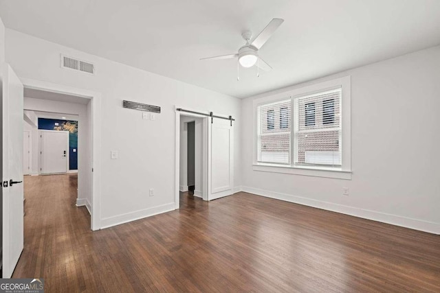 unfurnished bedroom featuring a barn door, ceiling fan, and dark hardwood / wood-style flooring