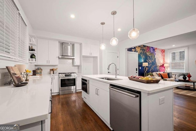 kitchen with stainless steel appliances, decorative light fixtures, a center island, sink, and wall chimney range hood