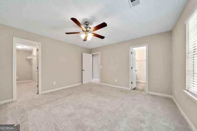 unfurnished bedroom with a spacious closet, ceiling fan, light colored carpet, and a closet