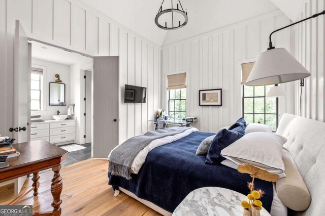 bedroom featuring light hardwood / wood-style floors, multiple windows, ensuite bath, and vaulted ceiling