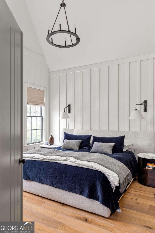 bedroom with light wood-type flooring, lofted ceiling, and a chandelier