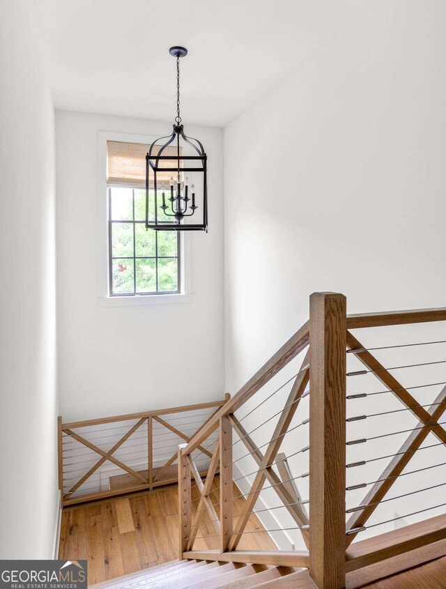 stairway with hardwood / wood-style floors and an inviting chandelier