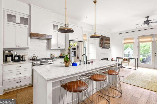 kitchen featuring a center island with sink, appliances with stainless steel finishes, pendant lighting, light stone countertops, and light wood-type flooring