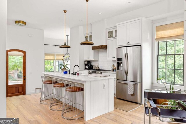 kitchen with hanging light fixtures, stainless steel fridge with ice dispenser, light hardwood / wood-style floors, and a kitchen island with sink