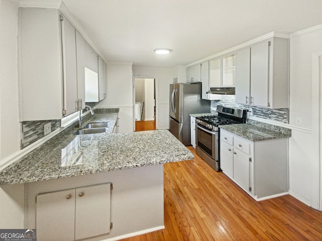 kitchen with appliances with stainless steel finishes, light hardwood / wood-style floors, kitchen peninsula, sink, and light stone counters