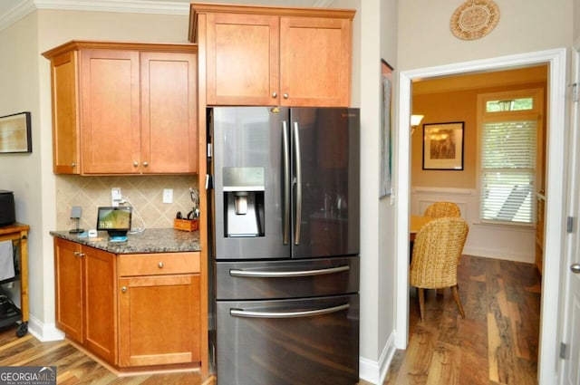 kitchen featuring stainless steel fridge, decorative backsplash, hardwood / wood-style flooring, dark stone countertops, and crown molding