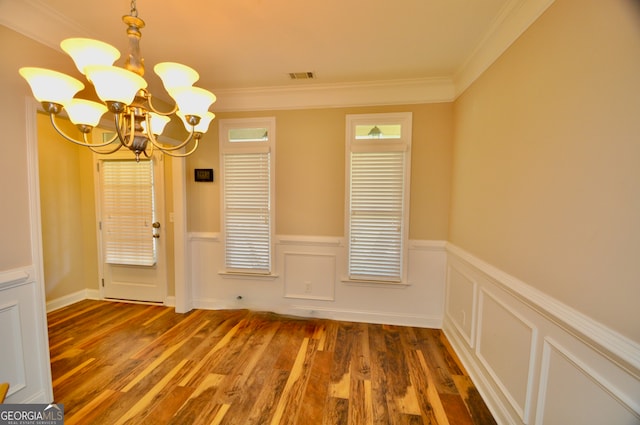 unfurnished dining area featuring an inviting chandelier, ornamental molding, and dark hardwood / wood-style floors