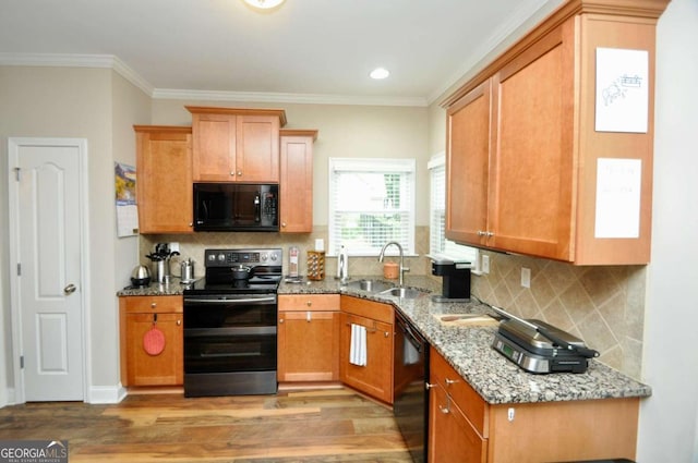 kitchen with light stone countertops, light hardwood / wood-style flooring, ornamental molding, black appliances, and sink