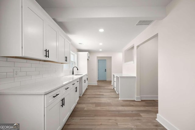 kitchen with light stone countertops, backsplash, light hardwood / wood-style floors, sink, and white cabinetry