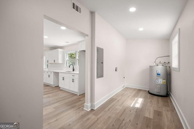 washroom with electric water heater, light hardwood / wood-style flooring, electric panel, and sink