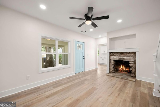 unfurnished living room featuring ceiling fan, light hardwood / wood-style floors, and a stone fireplace