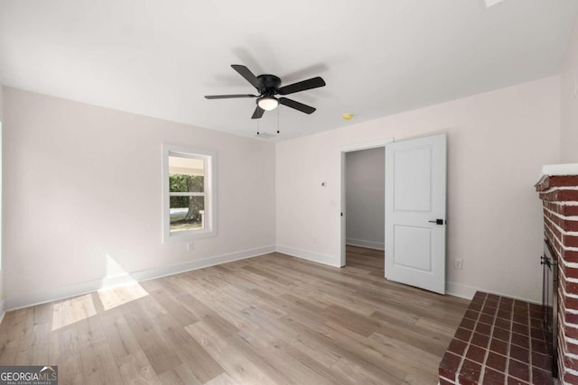 interior space featuring ceiling fan, light wood-type flooring, and a brick fireplace