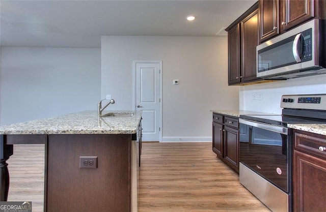 kitchen featuring dark brown cabinets, light hardwood / wood-style floors, sink, stainless steel appliances, and a center island with sink