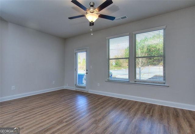 spare room featuring a healthy amount of sunlight, dark wood-type flooring, and ceiling fan