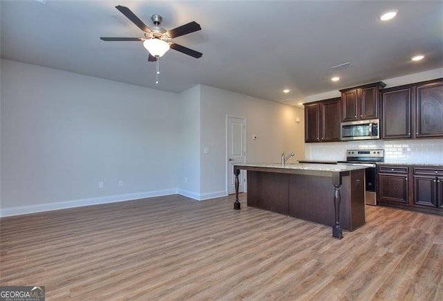 kitchen with appliances with stainless steel finishes, light hardwood / wood-style floors, an island with sink, a breakfast bar area, and ceiling fan