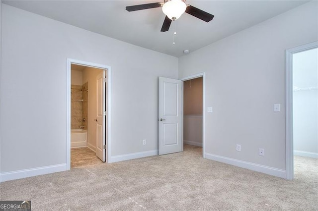 unfurnished bedroom with ceiling fan, a closet, a spacious closet, light carpet, and ensuite bath