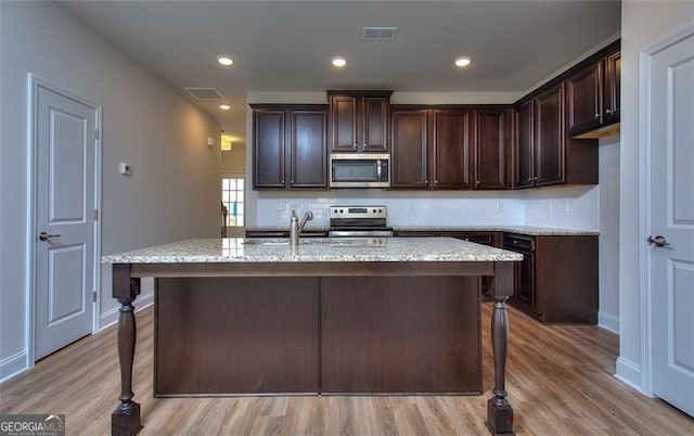 kitchen with light wood-type flooring, a center island with sink, stainless steel appliances, and light stone counters