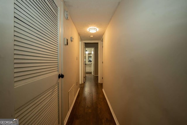 corridor featuring a textured ceiling and dark hardwood / wood-style flooring