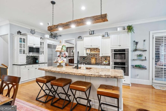 kitchen with built in appliances, an island with sink, white cabinets, and tasteful backsplash