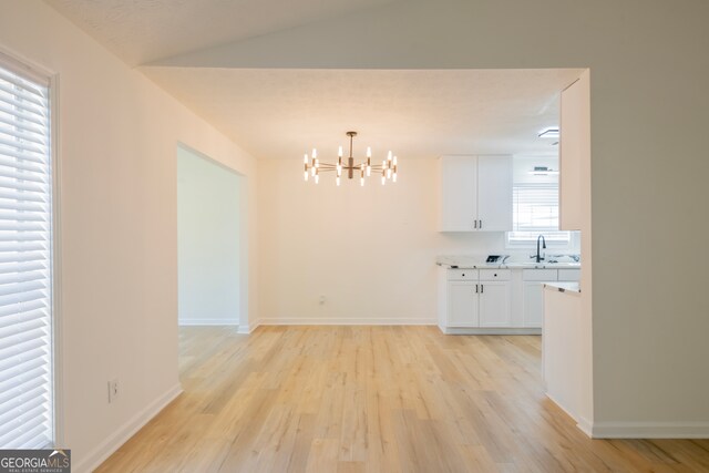 unfurnished dining area with vaulted ceiling, sink, and light wood-type flooring