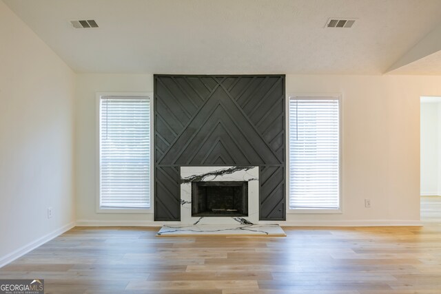 unfurnished living room featuring plenty of natural light, a large fireplace, light wood-type flooring, and lofted ceiling