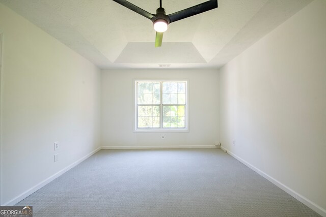 carpeted spare room with a raised ceiling and ceiling fan