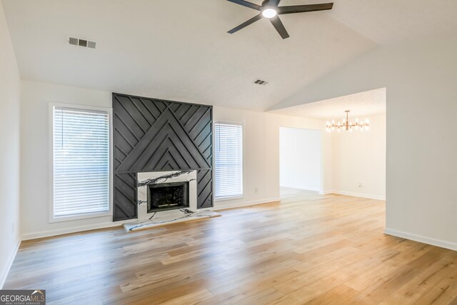 unfurnished living room with ceiling fan with notable chandelier, lofted ceiling, a large fireplace, and light hardwood / wood-style floors