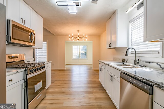 kitchen featuring light hardwood / wood-style flooring, light stone counters, stainless steel appliances, a notable chandelier, and white cabinetry