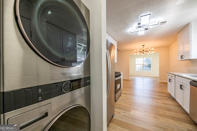 laundry room with stacked washer and clothes dryer, a textured ceiling, and light hardwood / wood-style flooring