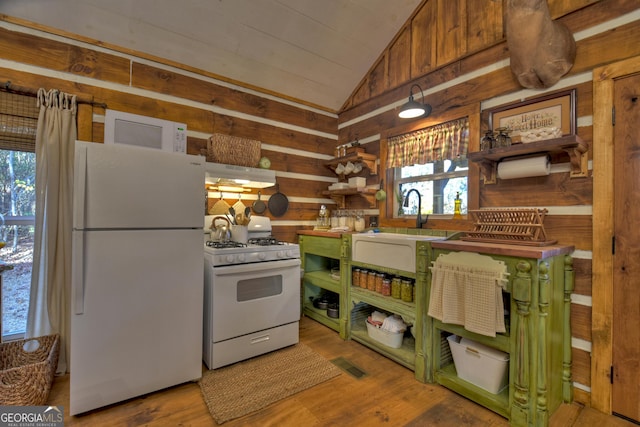 kitchen featuring white appliances, light wood-type flooring, wooden walls, sink, and vaulted ceiling