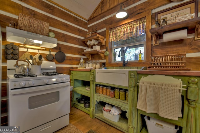 kitchen with lofted ceiling, wood walls, white gas stove, and light hardwood / wood-style flooring