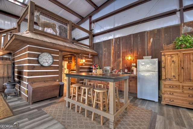 interior space featuring a kitchen breakfast bar, refrigerator, dark hardwood / wood-style floors, and wooden walls