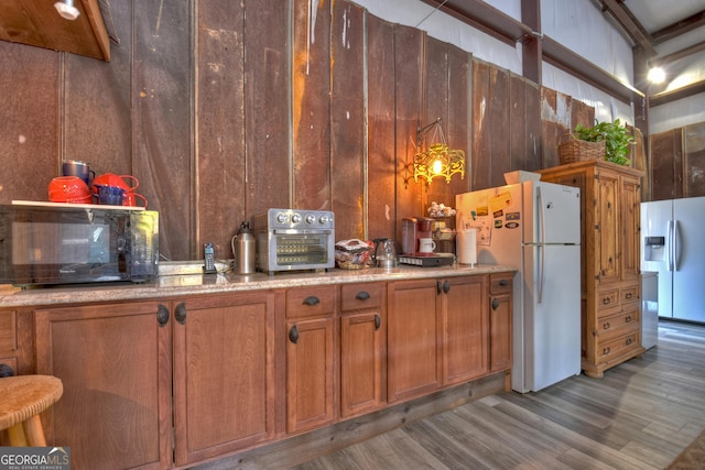 kitchen featuring light wood-type flooring, white refrigerator, refrigerator with ice dispenser, and wooden walls