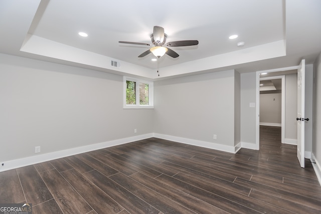 empty room featuring a raised ceiling, ceiling fan, and dark hardwood / wood-style flooring