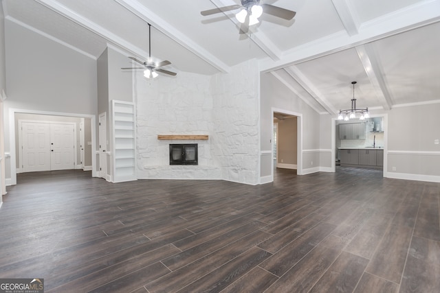 unfurnished living room with dark hardwood / wood-style floors, ceiling fan with notable chandelier, a stone fireplace, sink, and lofted ceiling with beams