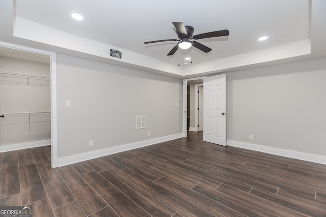 unfurnished bedroom with a walk in closet, a raised ceiling, ceiling fan, and dark hardwood / wood-style floors