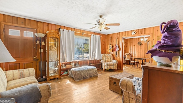 interior space with ceiling fan, light hardwood / wood-style floors, crown molding, wood walls, and a textured ceiling