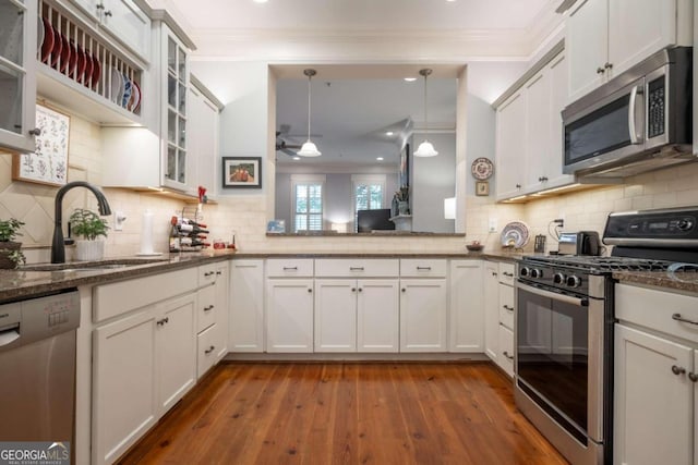 kitchen featuring decorative light fixtures, wood-type flooring, stainless steel appliances, sink, and white cabinets