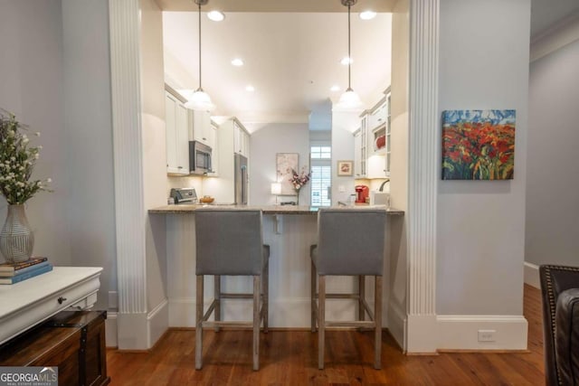 kitchen featuring stainless steel appliances, white cabinetry, dark wood-type flooring, pendant lighting, and a kitchen bar