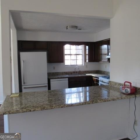 kitchen featuring white appliances, light stone counters, kitchen peninsula, and sink