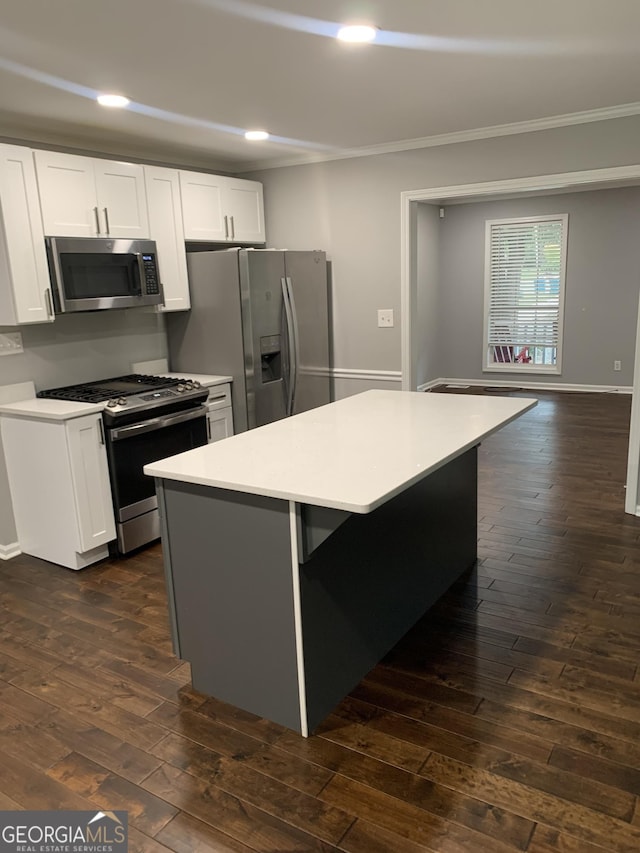 kitchen featuring appliances with stainless steel finishes, dark wood-type flooring, crown molding, a center island, and white cabinetry