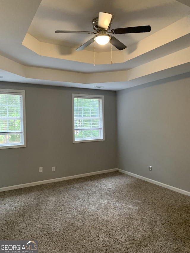 carpeted spare room with a raised ceiling, plenty of natural light, and ceiling fan