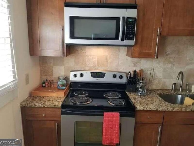 kitchen featuring light stone counters, stainless steel appliances, sink, and decorative backsplash